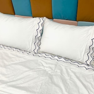 May include: Two white pillowcases with a scalloped edge and black trim on a white bed.