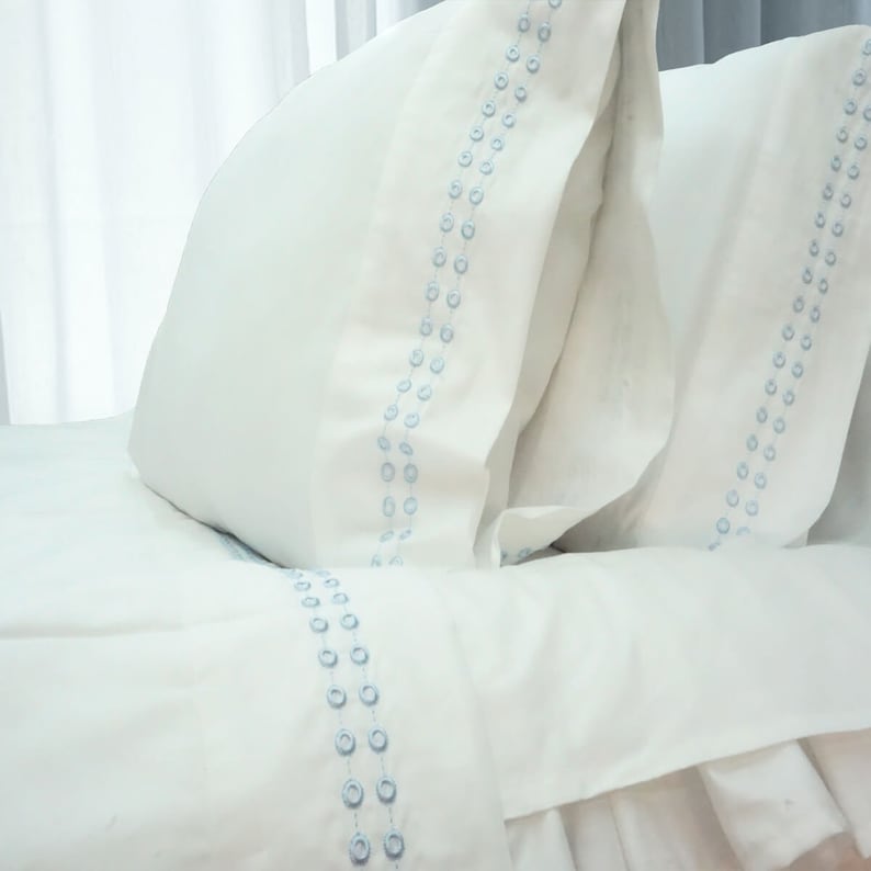 May include: White bedding with a light blue embroidered design. The bedding features a decorative stitch pattern of small circles.