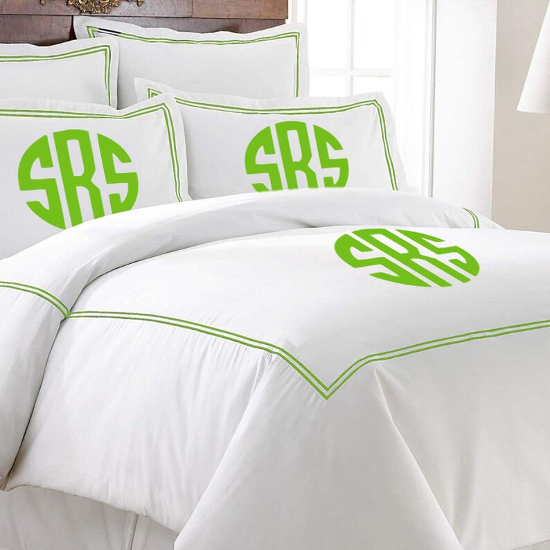 K&ouml;nnte beinhalten: Wei&szlig;es Bettw&auml;sche-Set mit gr&uuml;nen Zierleisten und Monogramm. Das Set beinhaltet einen Bettbezug und Kissenbez&uuml;ge, alle mit den Initialen "SRS" in leuchtendem Gr&uuml;n. Die Bettw&auml;sche hat ein sauberes, frisches Aussehen.