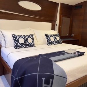 Può includere: Un letto bianco con una testiera bianca e una coperta blu navy e grigia. Il letto ha due cuscini bianchi con cuscini a motivi blu navy e bianchi sopra.