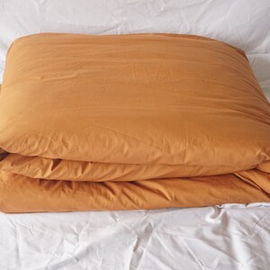 May include: A folded mustard yellow duvet cover on a white bed.