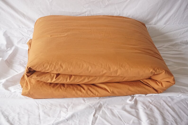 May include: A folded mustard yellow duvet cover on a white bed.