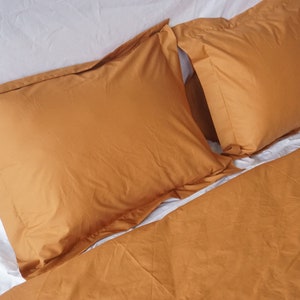 May include: Two rust-colored pillowcases on a white bed with a rust-colored duvet cover.