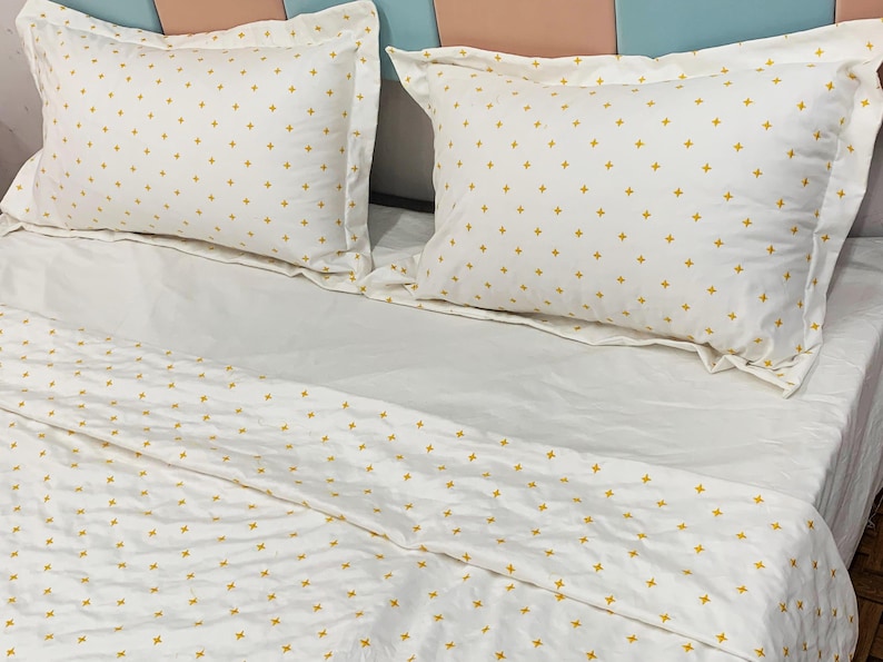 May include: White bed linen set featuring a repeating pattern of small yellow crosses. The set includes two pillowcases and a fitted sheet. The pillowcases have a ruffled edge. The bed is made up and ready for use.