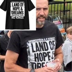 May include: A black short-sleeved t-shirt featuring a white rectangular graphic with the text "SPRINGSTEEN E STREET LAND OF HOPE & DREAMS AMERICAN TOUR NO KINGS" printed in bold black lettering across the chest area of the garment.