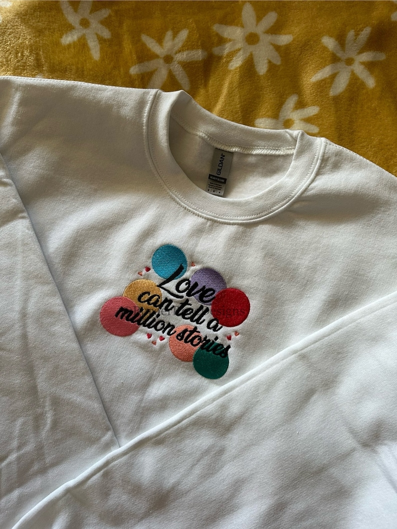 May include: White sweatshirt with a colorful embroidered design that says "Love can tell a million stories".