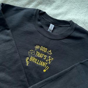 Peut inclure: Sweat-shirt noir avec un texte brodé en jaune qui dit "God that's brilliant!" avec différentes icônes autour du texte.
