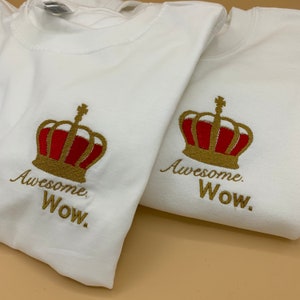 Puede incluir: Dos camisetas blancas con coronas bordadas en dorado y el texto "Awesome. Wow."
