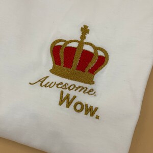 Puede incluir: Camiseta blanca con bordado dorado de una corona y el texto "Awesome. WOW."
