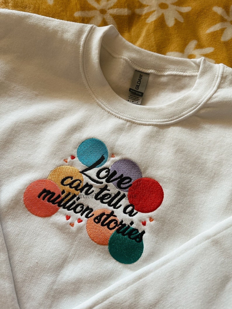 May include: White sweatshirt with colorful embroidered circles and the text "Love can tell a million stories".