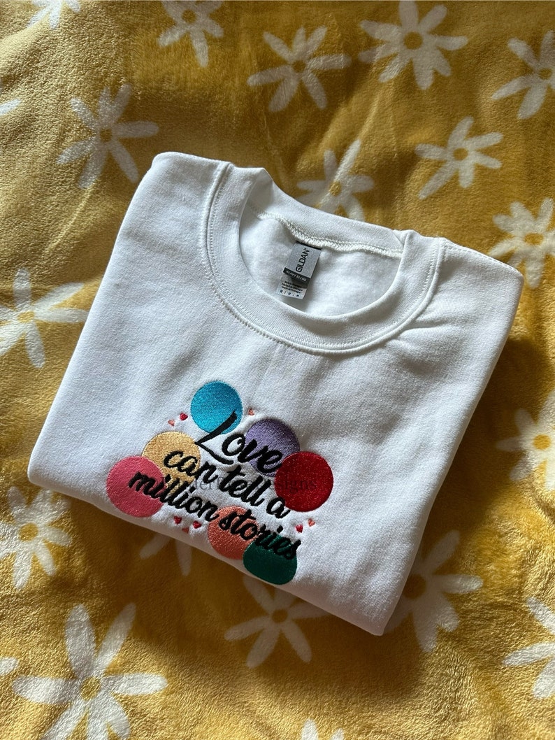 May include: White sweatshirt with a colorful embroidered design that says "Love can tell a million stories".
