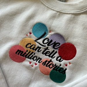 May include: White sweatshirt with embroidered colorful circles and the text "Love can tell a million stories".