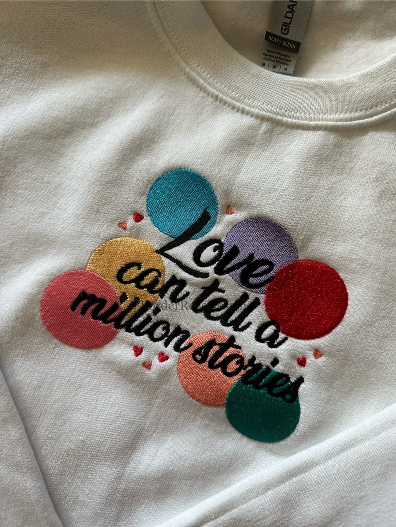 May include: White sweatshirt with embroidered colorful circles and the text "Love can tell a million stories".