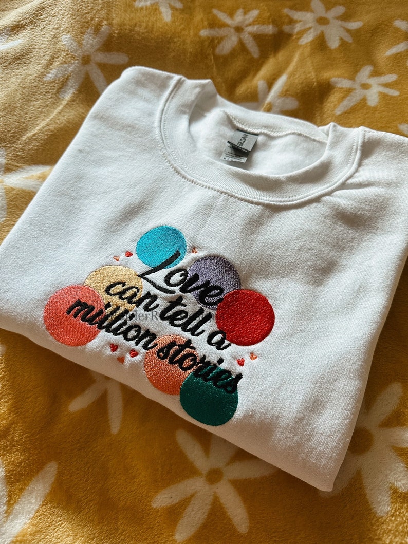 May include: White sweatshirt with colorful embroidered circles and the text "Love can tell a million stories".