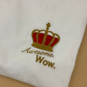 Puede incluir: Camiseta blanca con bordado dorado de una corona y el texto "Awesome. WOW."