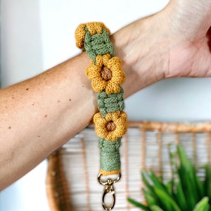 May include: A green and yellow crocheted keychain with a sunflower design and a gold metal clasp.