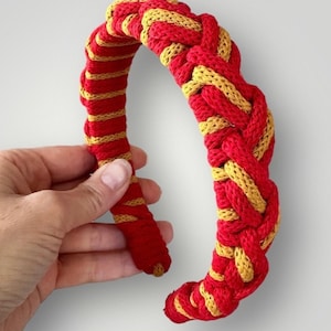 May include: A red and gold braided headband. The headband is made of a thick, woven fabric.