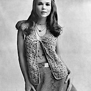 May include: A woman wearing a crocheted vest with a tie front and a mini skirt. She is wearing multiple necklaces.