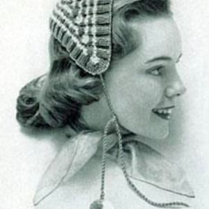 Puede incluir: Un gorro de crochet blanco y gris con un patrón geométrico. El gorro tiene dos cordones largos con cuentas blancas y grises en los extremos.