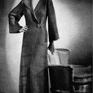 May include: A vintage, floor-length coat with a shawl collar and flared sleeves. The coat is cinched at the waist with a decorative clasp. The image is in black and white, evoking a classic, retro style. The coat appears to be made of a textured fabric.