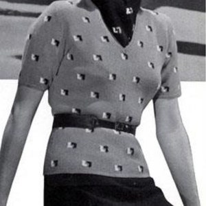 May include: A light gray V-neck sweater with short sleeves, adorned with a repeating pattern of small black and white squares. A black scarf and belt complete the outfit, paired with a dark skirt.
