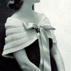 Peut inclure: Une femme portant un châle blanc à plusieurs couches en forme de nœud sur une robe noire. Le châle est noué au cou avec un grand nœud.