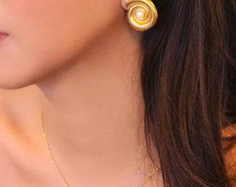 May include: A gold necklace with a small pearl cluster pendant. The necklace is worn by a person with long brown hair and gold earrings with a pearl accent.