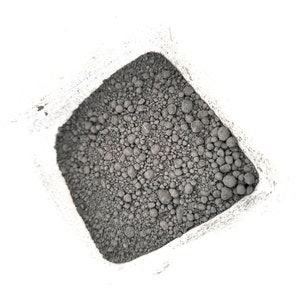 Puede incluir: Vista de cerca de un pequeño contenedor blanco lleno de material redondo de color gris oscuro, parecido a guijarros.