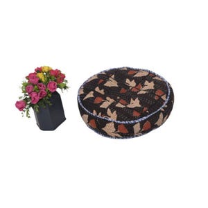 Puede incluir: Un cojín redondo estampado con un fondo oscuro y un diseño de hojas, junto a un jarrón negro con rosas rosas, amarillas y rojas. El cojín tiene un ribete azul.