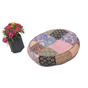 Peut inclure: Un coussin de sol en patchwork avec une variété de carrés de tissu à motifs dans les tons de rose, vert, bleu et marron. Un vase gris foncé contient un bouquet de roses roses et jaunes.