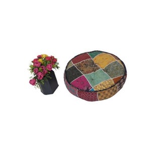 Könnte beinhalten: Ein runder Patchwork-Bodenkissen mit einer Vielzahl farbiger Stoffquadrate. Neben dem Kissen steht eine schwarze Vase mit rosa und gelben Rosen.
