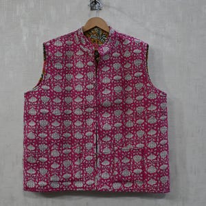 Puede incluir: Chaqueta sin mangas acolchada en un vibrante fucsia, adornada con un estampado floral repetido en blanco. La chaqueta presenta un cuello mandarín y una cremallera de largo completo. El reverso tiene un estampado floral amarillo y verde.