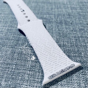 May include: White silicone Apple Watch band with a textured surface. The band has a white buckle and is designed for the Apple Watch.