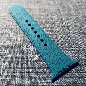 May include: Teal blue silicone watch band with a hexagonal pattern. The band has five holes for adjusting the fit.