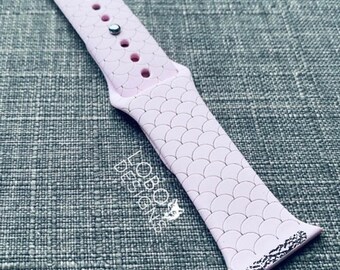 May include: A pink silicone watch band with a mermaid scale pattern. The band has a silver buckle and is designed for Apple Watches.