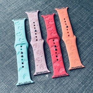 May include: Three Apple Watch bands in different colors: light blue, pink, and coral. Each band has a heart pattern and the words "Smile", "Kiss Me", and "You Are Love" embossed on the pink band.
