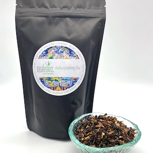 May include: A black resealable pouch of Maharaja Oolong Chai tea with a colorful label that reads "tealeavz" and lists the ingredients: "cooling tea, cinnamon, ginger, cardamom, chicory root, cloves". A glass bowl filled with loose leaf tea is in the foreground.