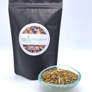 May include: A black pouch with a white label that reads "tealeavz. samurai spirit maté herbal tea". The pouch is open and a small glass bowl filled with loose leaf tea is in front of it.