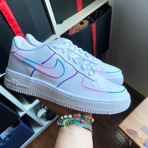 May include: White leather low-top sneakers with a pink, blue, and purple embroidered swoosh logo. The sneakers have a white rubber sole.