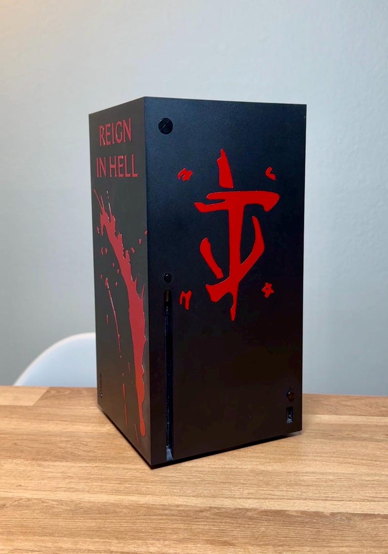 May include: A black gaming console with a red "REIGN IN HELL" text and a red Doom Slayer symbol on the front.