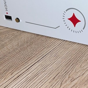 Op de afbeelding: Witte gameconsole met een rood sterlogo en het woord "UNCH" gedrukt op de zijkant. De console heeft een grijs-wit gestreept ontwerp.