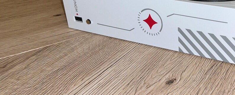 Op de afbeelding: Witte gameconsole met een rood sterlogo en het woord "UNCH" gedrukt op de zijkant. De console heeft een grijs-wit gestreept ontwerp.
