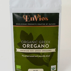 May include: A white resealable pouch with a green and black label. The label reads "Envios", "Wholesome Products Crafted by Nature", "Organic Greek Oregano", "Premium 100% Greek Oregano", "Hand harvested and naturally dried", "Net Wt. 40 g (1.41 oz)", and "USDA Organic".