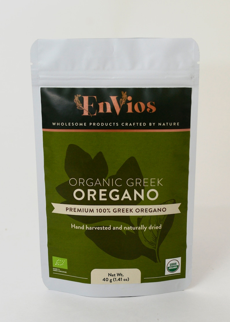 May include: A white resealable pouch with a green and black label. The label reads "Envios", "Wholesome Products Crafted by Nature", "Organic Greek Oregano", "Premium 100% Greek Oregano", "Hand harvested and naturally dried", "Net Wt. 40 g (1.41 oz)", and "USDA Organic".