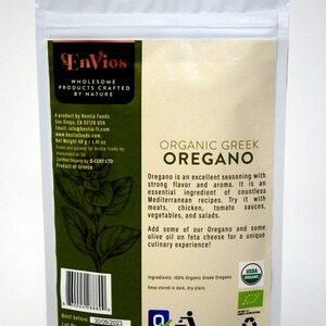 May include: A white resealable pouch with a green and brown label. The label reads "Envios Wholesome Products Crafted by Nature" and "Organic Greek Oregano". The label also includes a description of the product and its uses. The pouch is labeled with a USDA Organic seal.