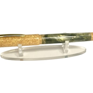 May include: A handcrafted pen with a gold-colored clip and a marbled green and tan barrel. The pen is displayed on a clear acrylic stand. The pen's barrel has a unique pattern, and the pen is designed for writing.