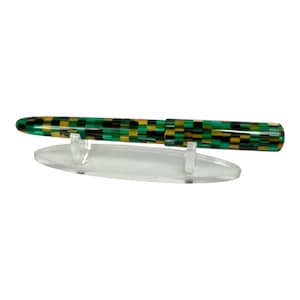 May include: A fountain pen with a checkerboard pattern in green, black, and gold. The pen is displayed on a clear plastic stand. The pen's design is a mix of colors and shapes.