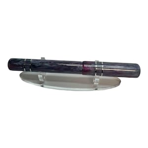 May include: A fountain pen with a marbled purple and dark grey resin body featuring silver-coloured metal bands. The pen rests horizontally on a clear, oval-shaped acrylic display stand designed to hold the writing instrument securely in place.