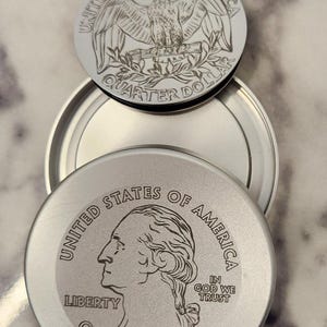 May include: Silver-colored jar lids with engraved designs. One lid features an eagle, the other a profile of George Washington, both with the words "United States of America" and "Quarter Dollar".