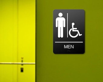 Può includere: Segnale del bagno rettangolare nero con pittogrammi bianchi per uomini e accessibilità in sedia a rotelle. La parola "MEN" è stampata in bianco sotto i pittogrammi. Il segnale è montato su un muro verde.